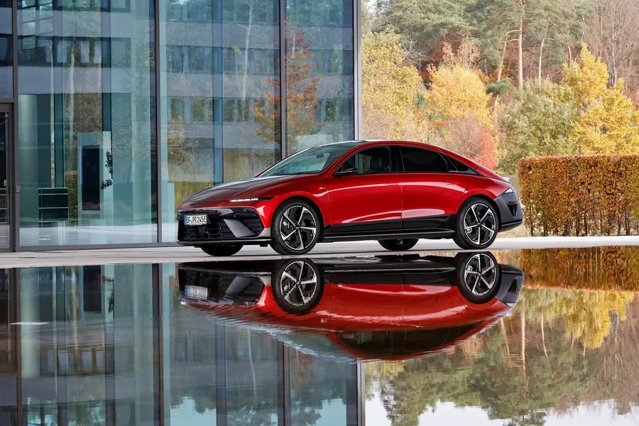 Red Hyundai Ioniq 6 N Line reflected in water beside a glass pavilion