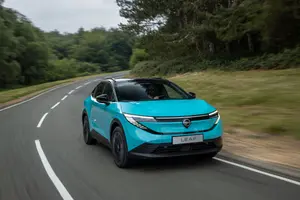 Turquoise Nissan Leaf with a black roof driving on a country road, front three-quarter view